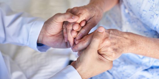 Hands of a man in a blue shirt holding those of an older woman in a blue dress