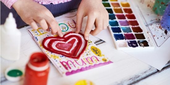 Child's hands making a card with a love heart that says 'I love you, Mum'