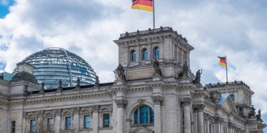 Ornate grey building with a glass dome and a German flag flying from the tower