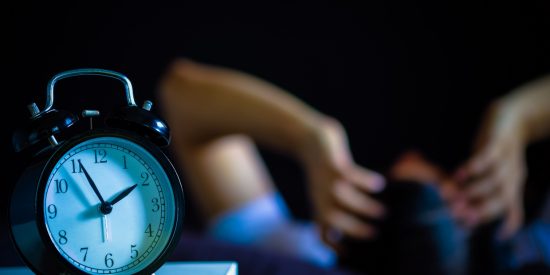 Clock displaying 1:55am with person having hands on head, struggling to sleep