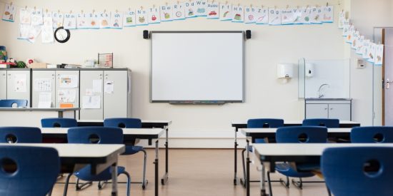 School classrom with whiteboard and blue chairs at rows of desks