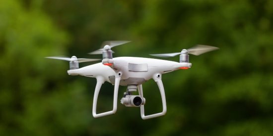 White drone whirring against a green background of trees