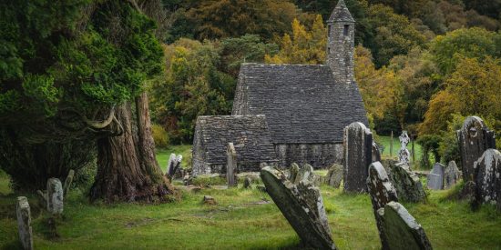 Small stone church with trees behind it and grave stones in front of it