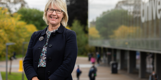 Professor Eeva Leinonen in a dark blazer stands in front of MU Library