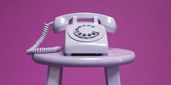 A purple rotary phone on a purple stool against a purple background