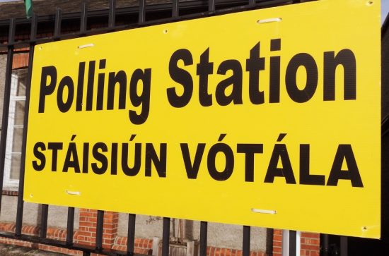 Large yellow sign hanging on railings outside a building that reads: Polling station/Stáisiún Vótála