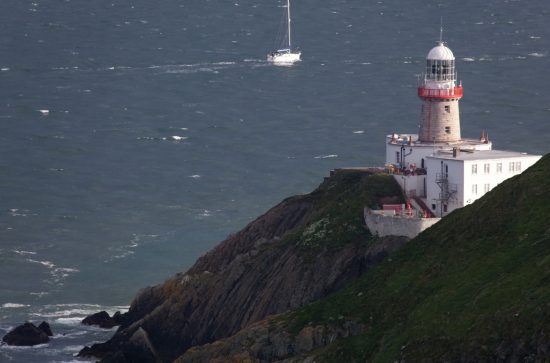 White and red lighthouse building sitting on a rocky outcrop with a boat approaching by sea