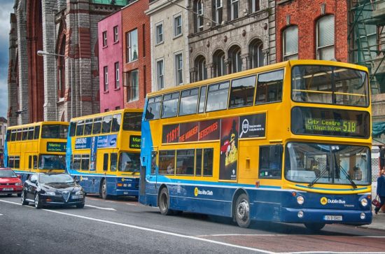 Three Dublin buses lined up on the street with cars passing by