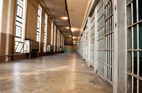 Prison corridor with row of cells separated from a row of windows by orange-floored walkway