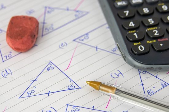 Lined piece of paper with triangles drawn on it and a red rubber, a biro and a calculator sitting on top of it