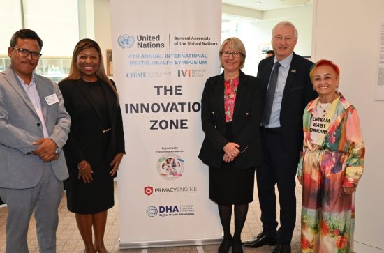 Man in a grey suit, woman in a black suit standing to the left of a banner that reads The Innovation Zone with a woman in a black suit and red blouse, a man in a black suit and a woman in a colourful outfit standing to the right