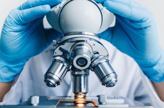 Person wearing blue gloves viewing a microscope