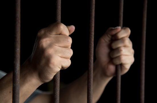 Man's hands gripping prison bars