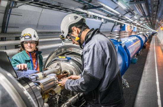 1 man and 1 woman in safety gear working on CERN's Hadron Collider