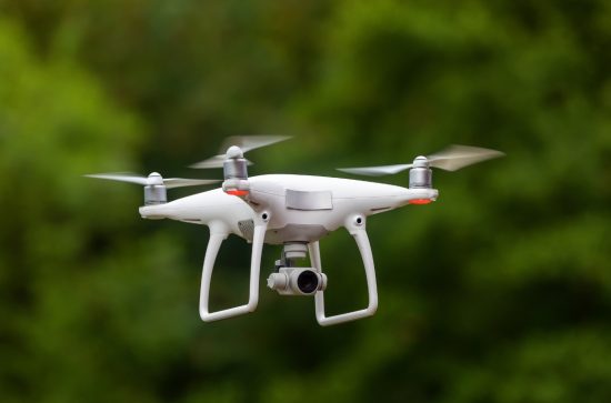 White drone whirring against a green background of trees